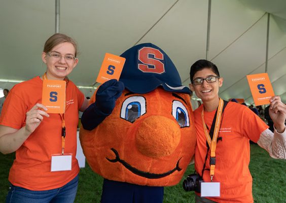 Mascot Otto with two students who are holding "passports"