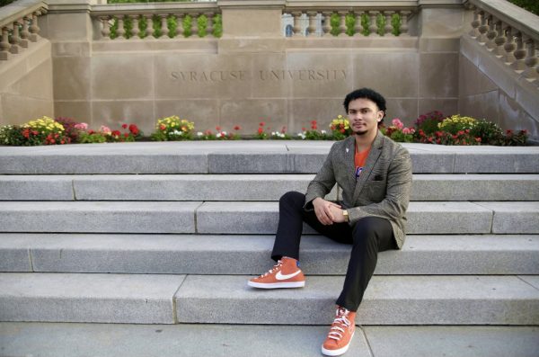 portrait of Hakim Morris sitting on the steps in front of the Syracuse University sign