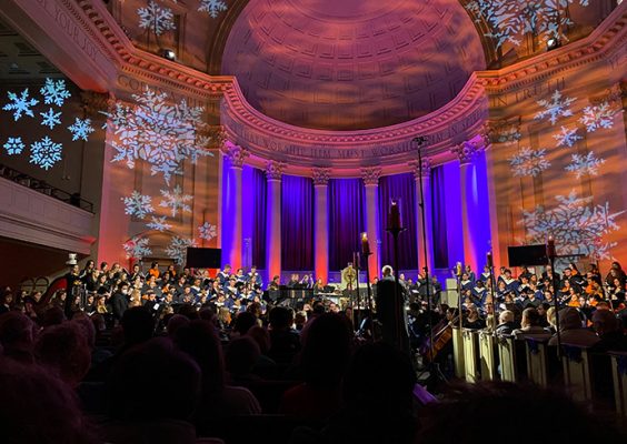 Hendricks Chapel lit up with orange and blue lighting while a chorus signs for an audience during Holidays at Hendricks.