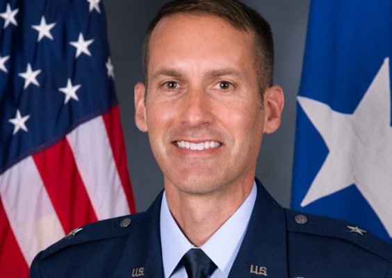 Man in Air Force dress smiling in front of the American flag.