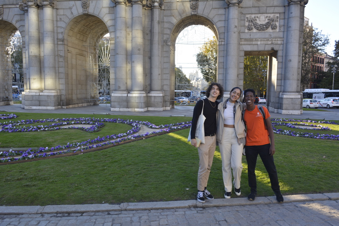 Tres estudiantes posan juntos frente a la Puerta de Alcalá en Madrid, España, mientras estudian en el extranjero