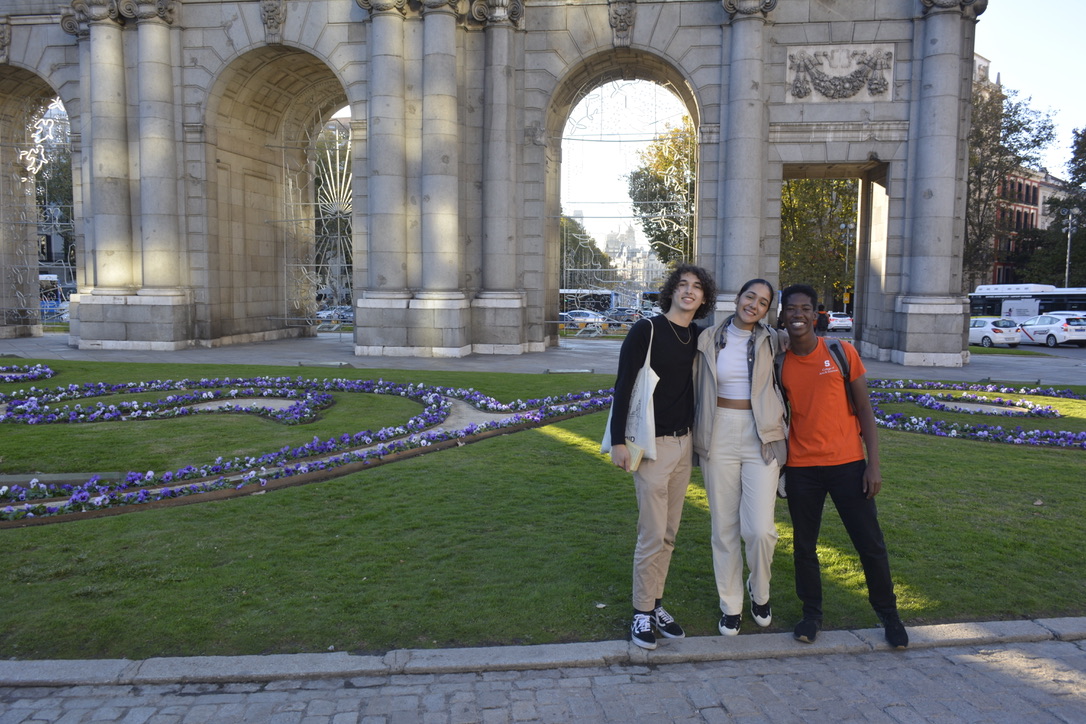 three students pose together in front of the Puerta de Alcalá in Madrid, Spain, while studying abroad