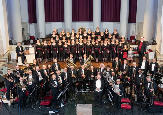 Large group of singers and musicians standing together in Hendricks Chapel.