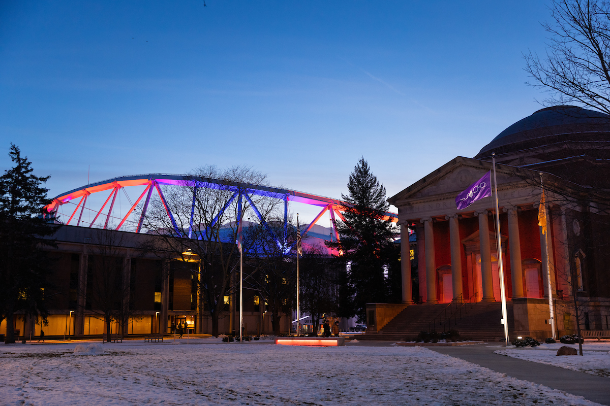Nighttime photo of campus buildings lit up in orange and blue