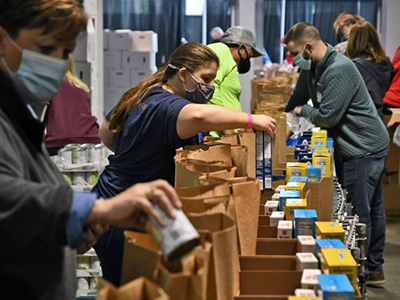 Several people putting food into a line of paper bags for a food drive.