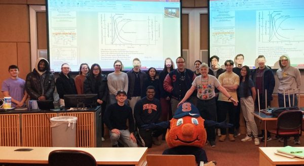 Group of individuals standing together in the front of a classroom with the Syracuse University mascot Otto the Orange