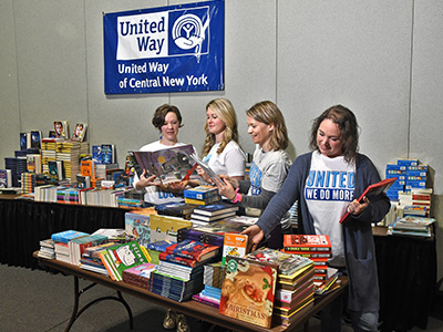 Four women standing together looking at and putting books together on a table for a book drive.