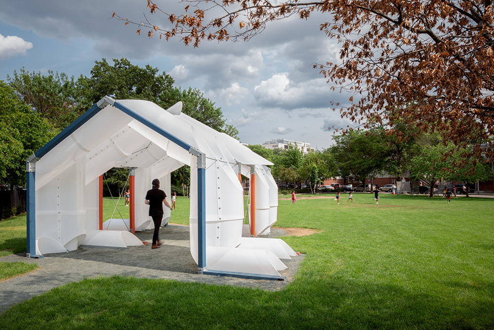 The CloudHouse, a shade pavilion in Cambridge Massachusetts. sits in a park-like setting with a person walking beneath it