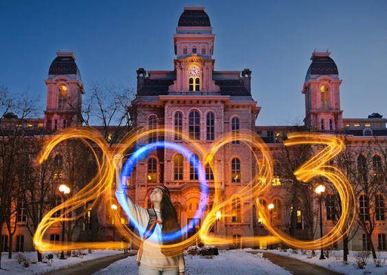 Individual standing in front of campus building using sparklers to write 2023