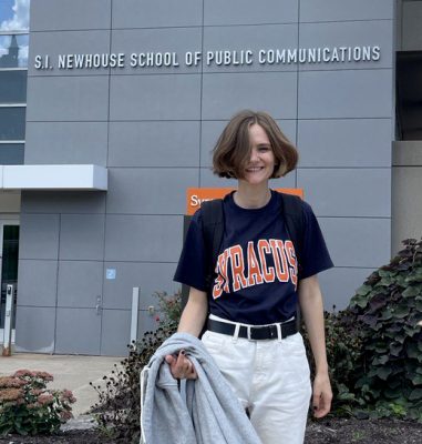 Woman smiling while wearing a blue Syracuse t-shirt outside of the Newhouse School.