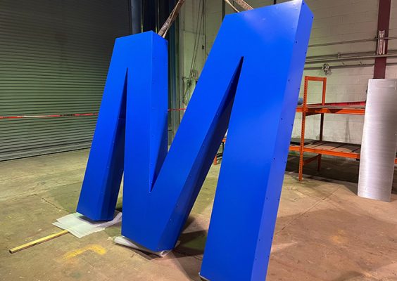 Giant steel letter "M" painted in blue.