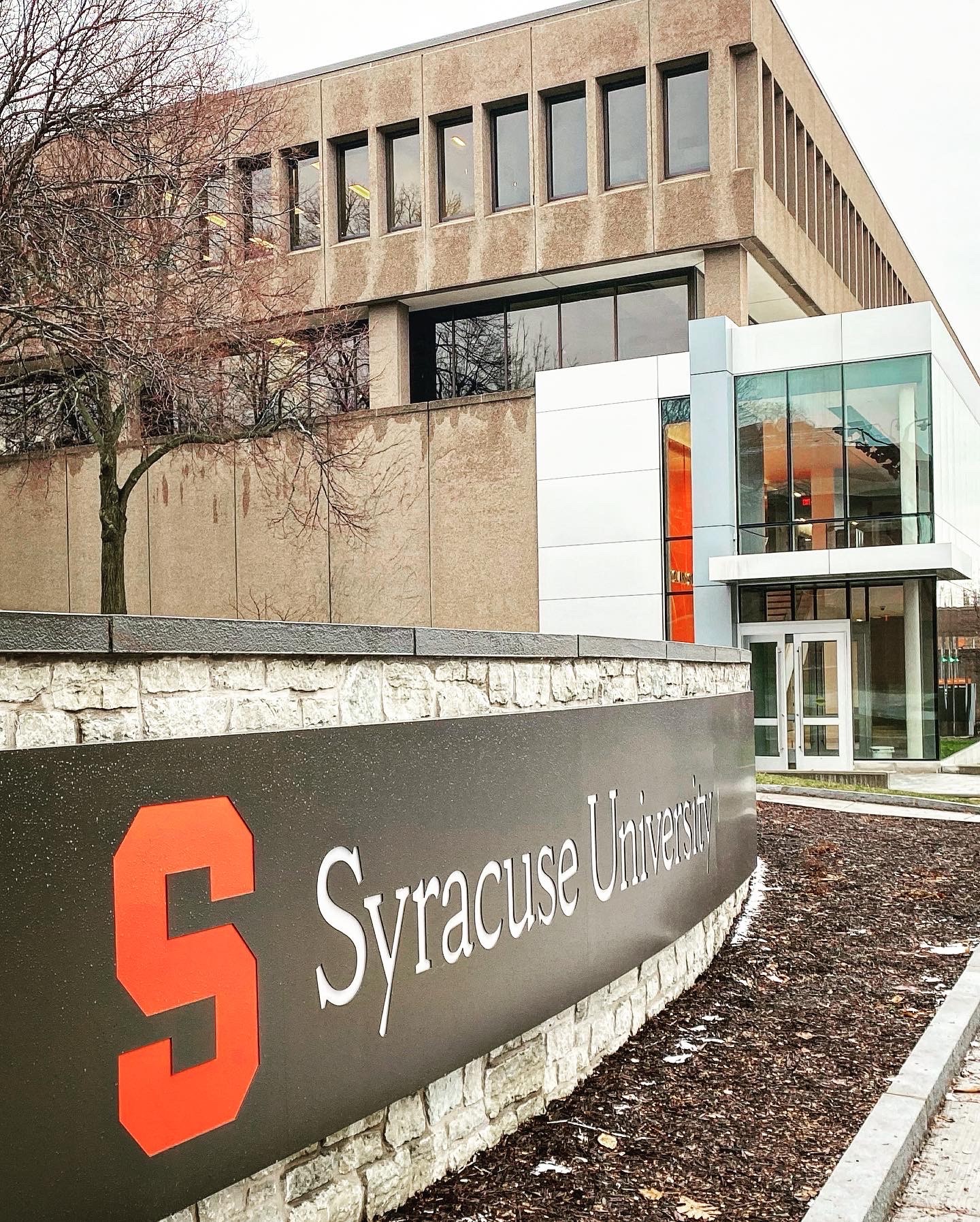 Syracuse University sign with the Newhouse building in the background.
