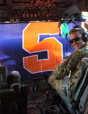 Lt. Col. Sean Stumpf smiles against the backdrop of a Syracuse flag hung in his military plane