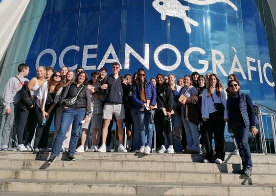 Group of students standing together on a set of stairs in front of a blue building with white lettering calling oceanographic.