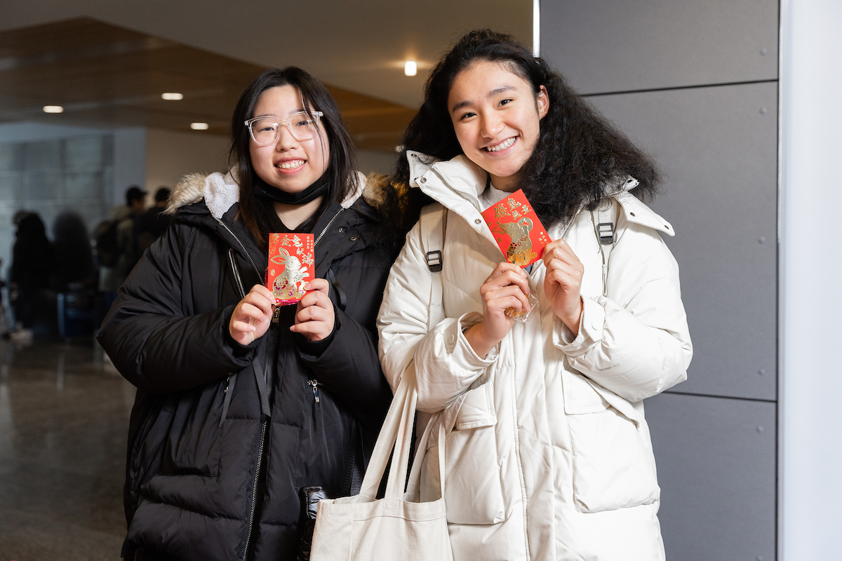 two students display red envelopes embossed with a rabbit design at the Newhouse School's Lunar New Year Celebration