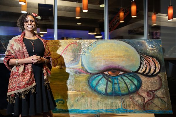 Artist Jessica McGhee poses with her painting, "Lexical Priming" at the 2023 MLK Celebration art exhibition in the JMA Wireless Dome