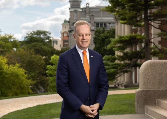 Portrait of Chancellor Kent Syverud smiling with university buildings and greenery in the background