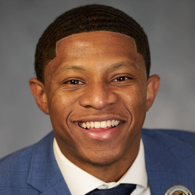 A man smiling indoors while wearing a shirt and tie.