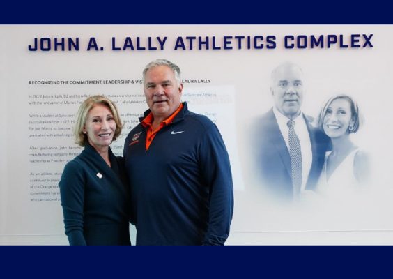 two people standing in front of a wall with a photo and the words John A. Lally Athletics Complex