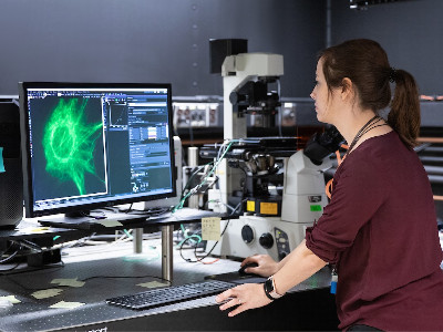 young woman looking at a green image on screen with a microscope