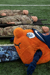 Otto the Orange laying on the field next to dummies dressed in camouflage 