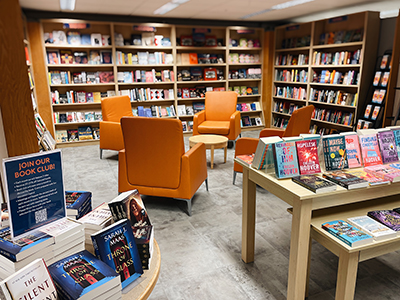 Area of the Campus Store with book shelves filled with books and orange chairs to sit at