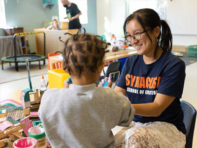 Person in a Syracuse School of Education t-shirt reads with a preschool student at a low table