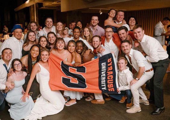 Large group of people standing together at a wedding holding a Syracuse flag.