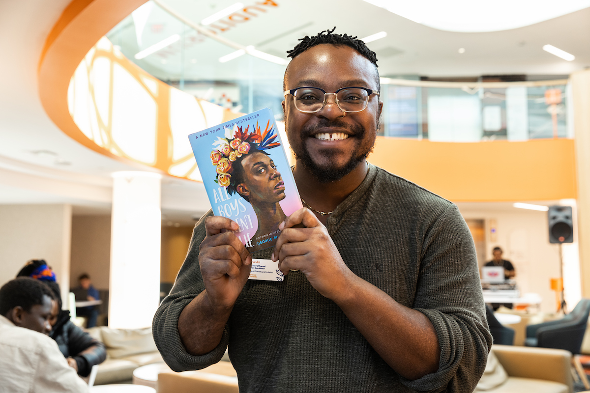 Staff member holds up a copy of the book "All Boys Aren't Blue" at the Black and Brown Information Fair in Schine Student Center