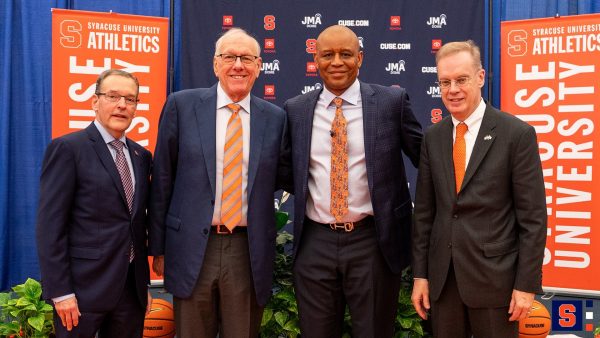 Four men standing in front of a backdrop reading Syracuse University athletics.