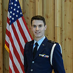 Man smiling standing next to American flag in a military uniform.