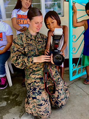 Individual in military uniform holding a camera showing an image to a child