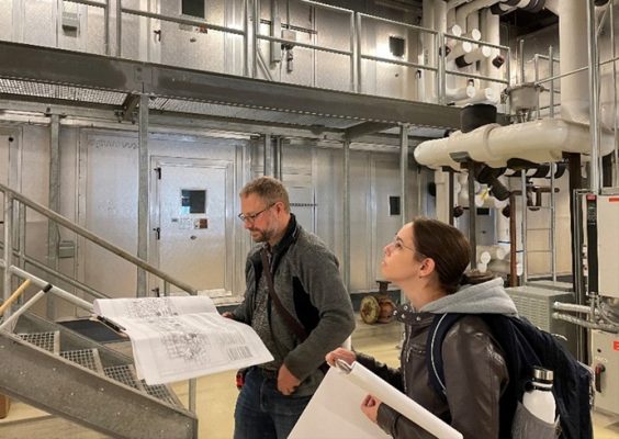 two engineers assess plans in the mechanical room of the Life Sciences Complex