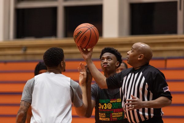 Referee holding up a basketball with players zoomed in on play at the annual Black History Month Basketball Classic