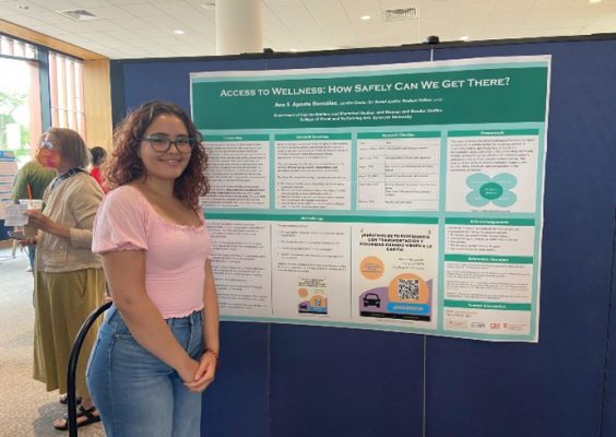 young woman looking at camera with a poster of her research work on display
