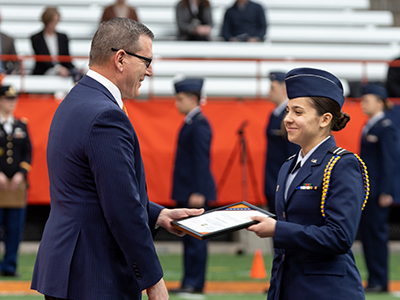 Person in military uniform accepting award from a person in a suit.