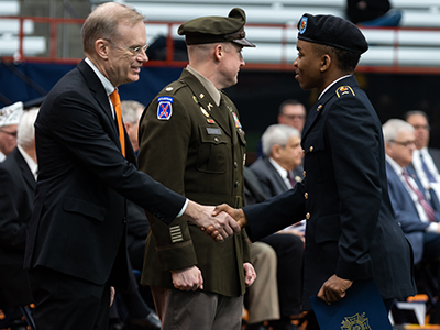 Person in military uniform shaking the hand of a person in a suit.