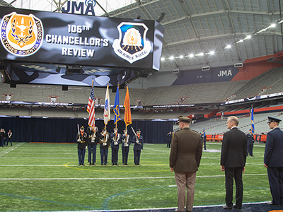 106th Chancellor's Review on field of the JMA Wireless Dome. Colors being presented with three individuals standing together facing the military persons presenting the colors.