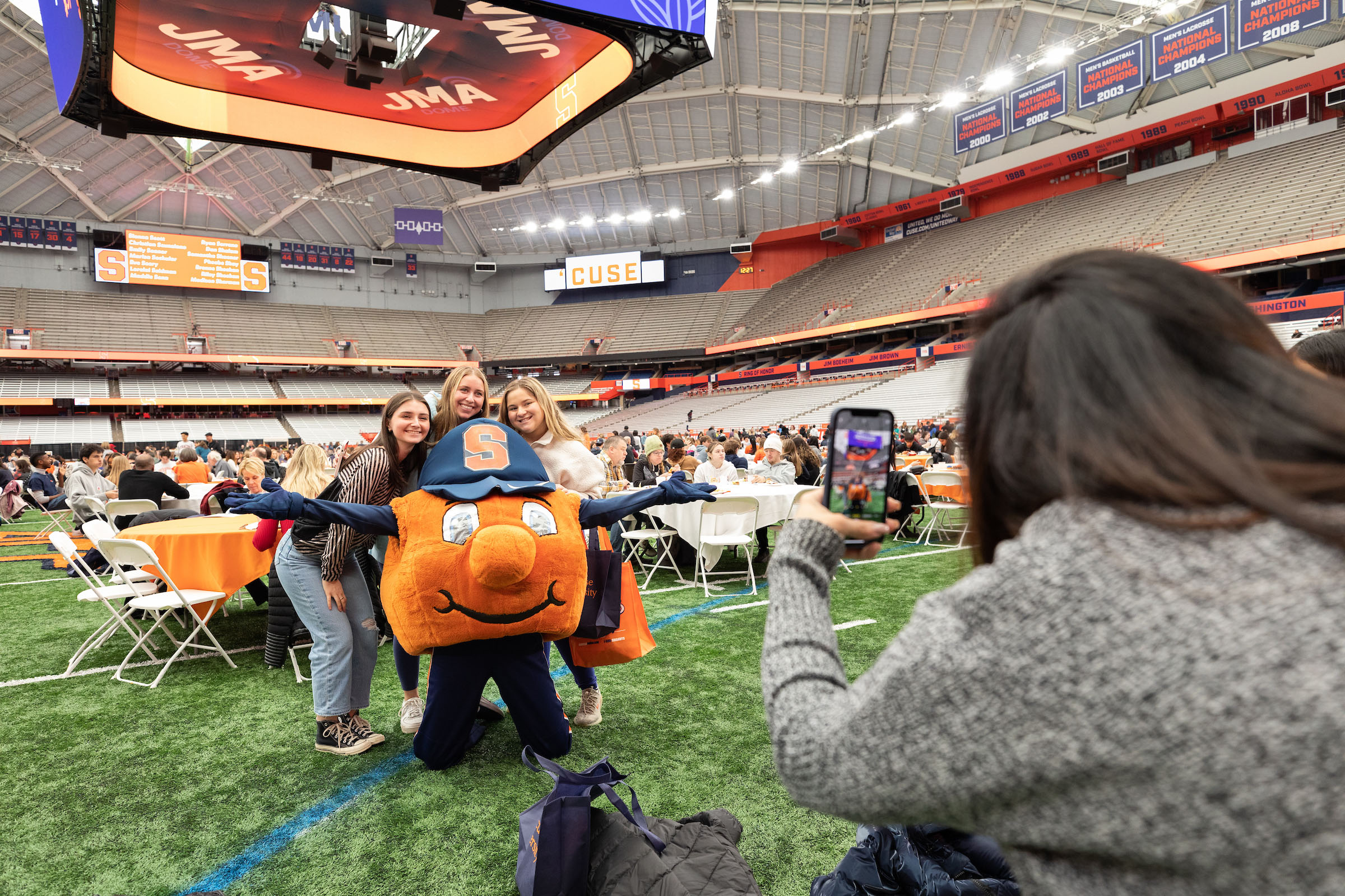 Students posing with Otto while someone was taking a photo on the floor of the JMA Wireless Dome.
