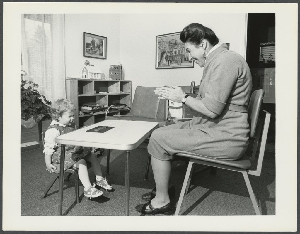 person seated talking to child at desk
