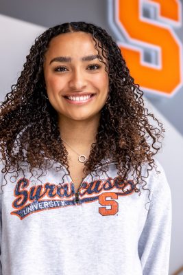 student Khloe Gage wearing a Syracuse sweatshirt and smiling in front of a Block S