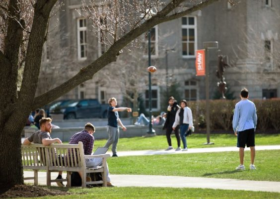 students relaxing tossing a football on campus