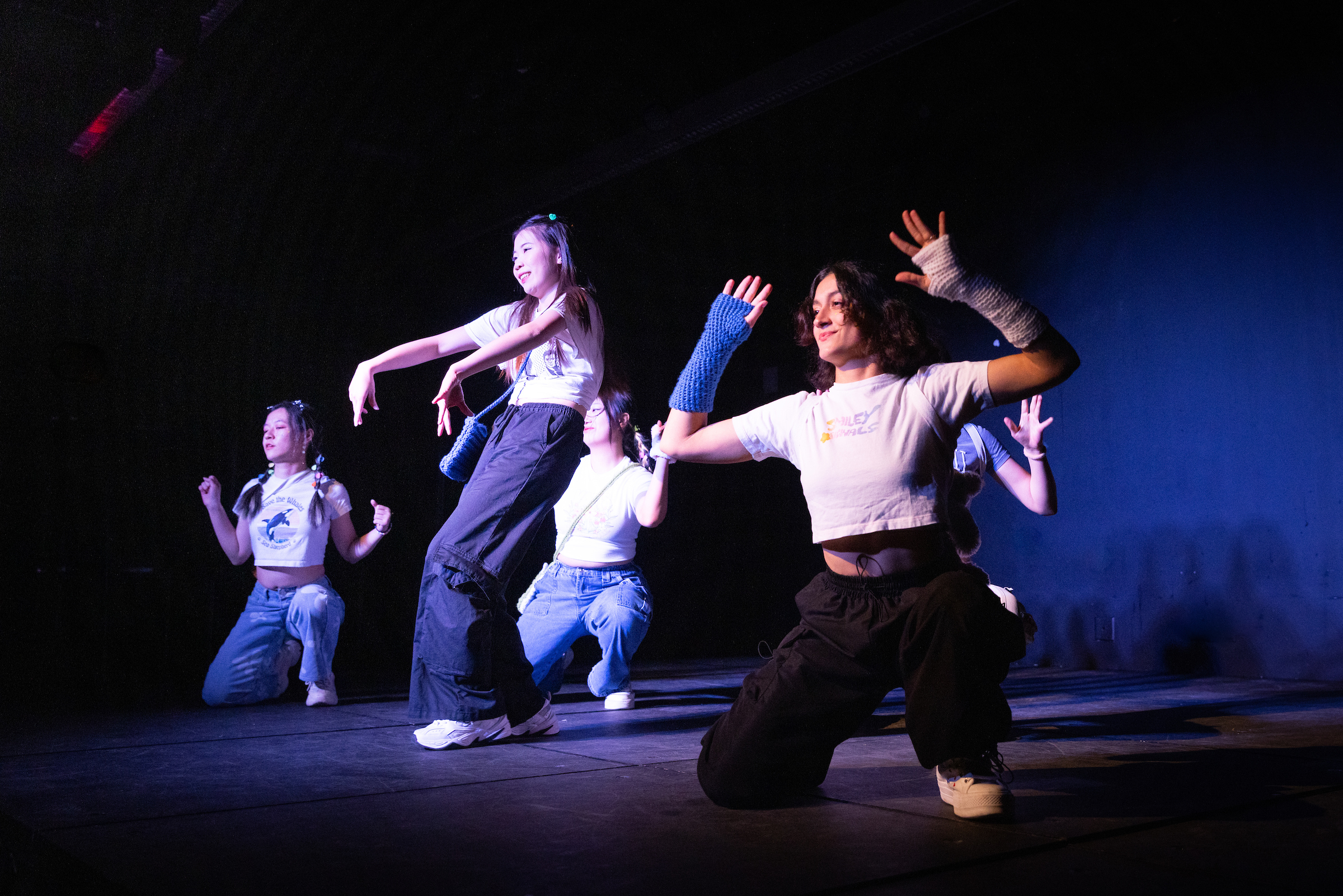 Five students dancing on a dark lit stage.