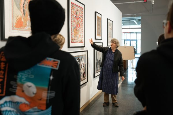 Woman pointing at a painting on a wall speaking in front of several others.