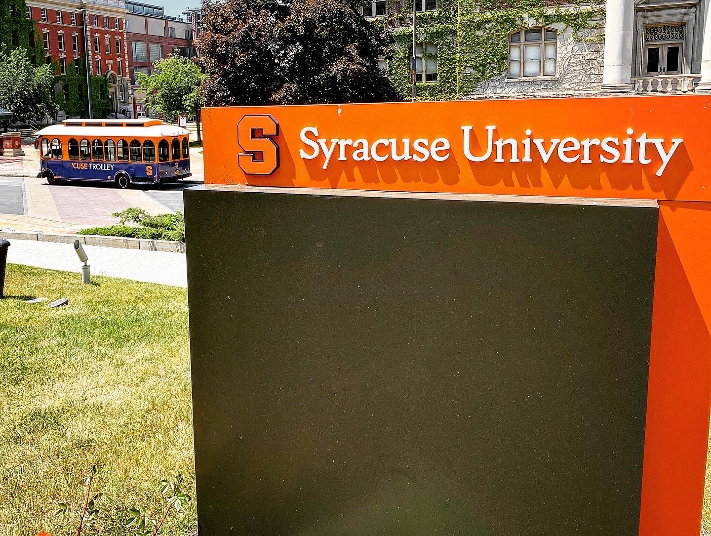 Syracuse University sign in the foreground and a Cuse Trolley in the background.