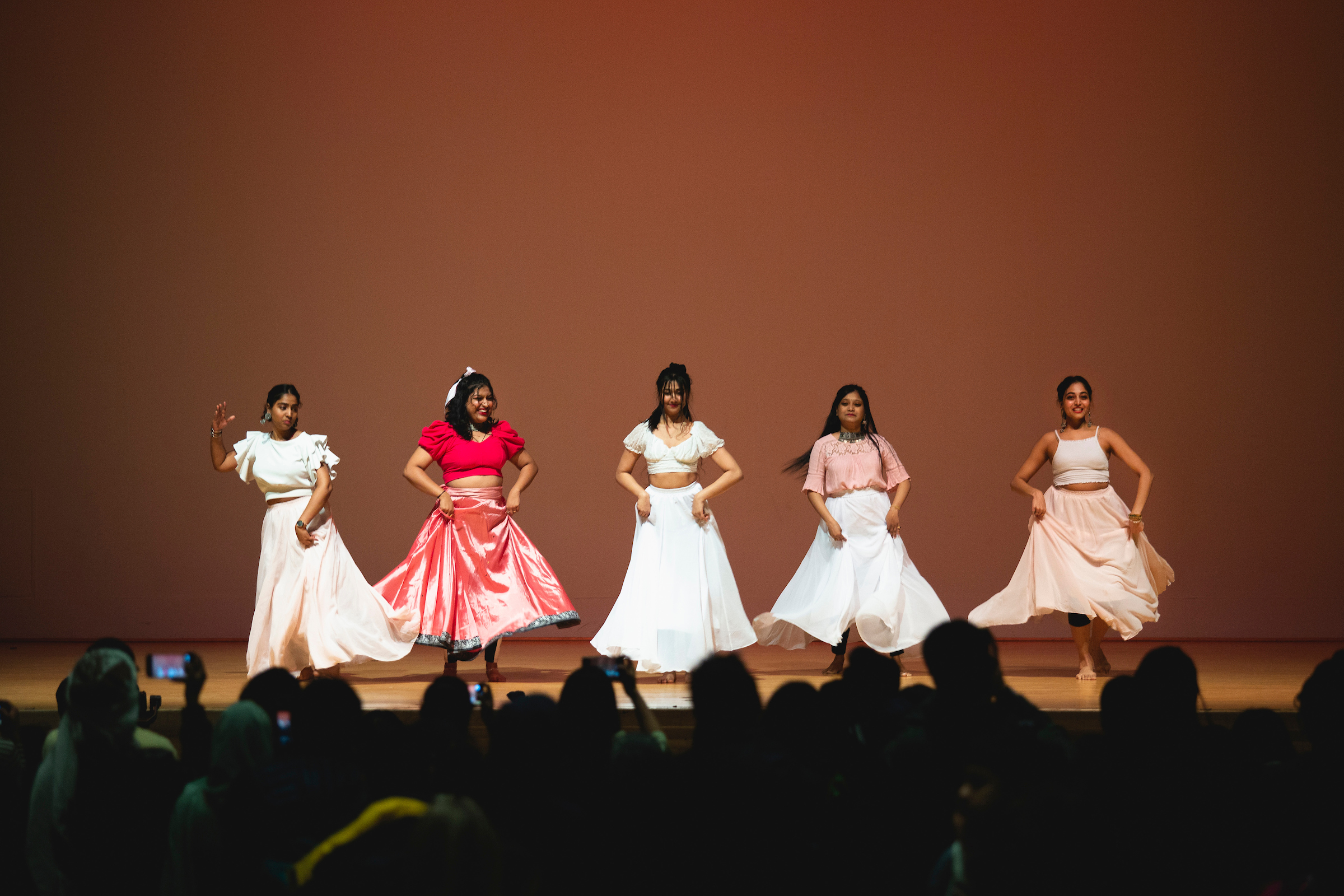 Group of five individuals on a stage dancing in red and white dresses