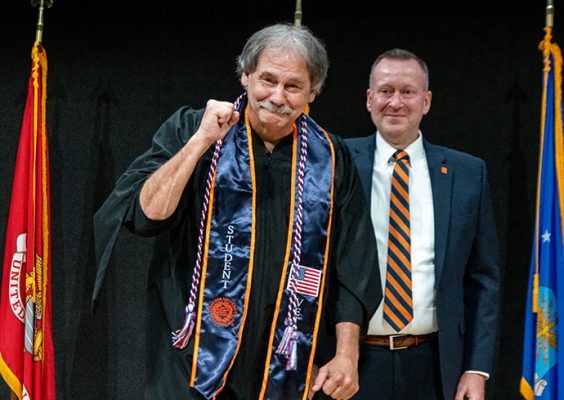 Man standing on stage smiling holding his arm up as a sign of accomplishment.
