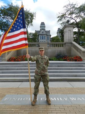 Air Force ROTC cadet Emily Weaver holds an American flag in uniform in front of the Hall of Languages
