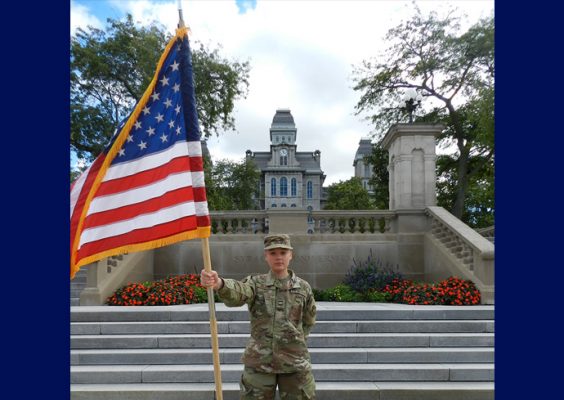 Air Force ROTC cadet Emily Weaver holds an American flag in uniform in front of the Hall of Languages