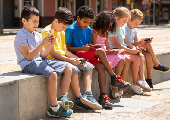 stock image of six children sitting outside looking at mobile devices